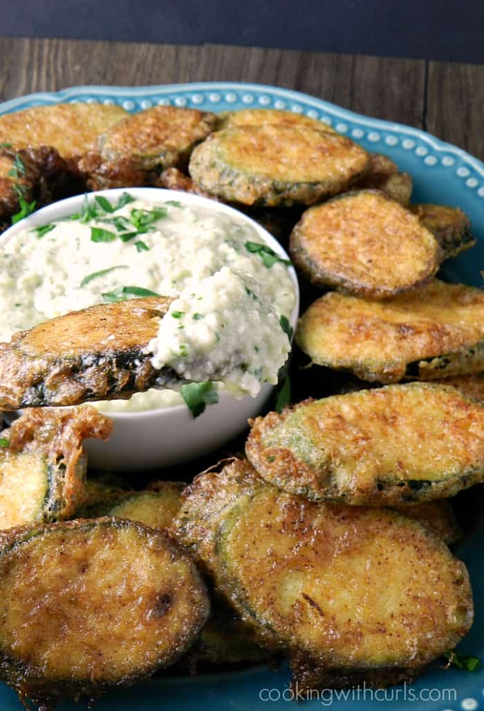 zucchini fritters on a blue plate with pine nut sauce for dipping in a small white bowl in the center