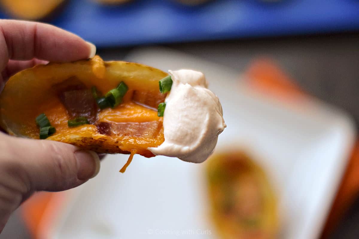 Hand holding baked potato skin dipped in sour cream.