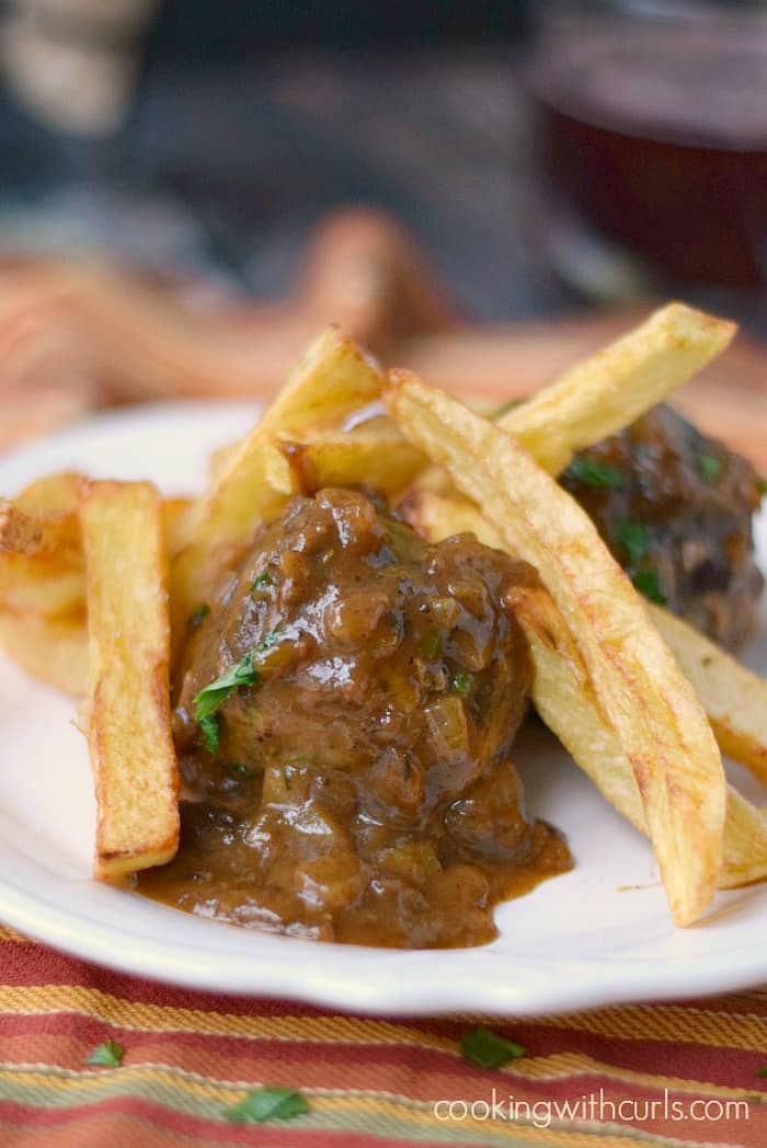 meatballs and french fries on a small white plate sitting on a multi-colored napkin.