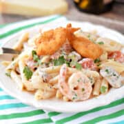 Penne pasta mixed with a creamy shrimp sauce, shrimp, mushrooms, tomatoes, and topped with three breaded shrimp on a white plate.