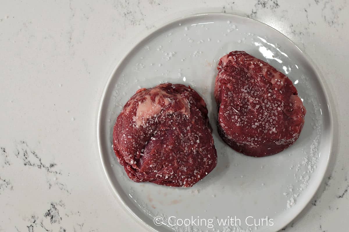 Two beef tenderloin filets covered with kosher salt on a plate. 