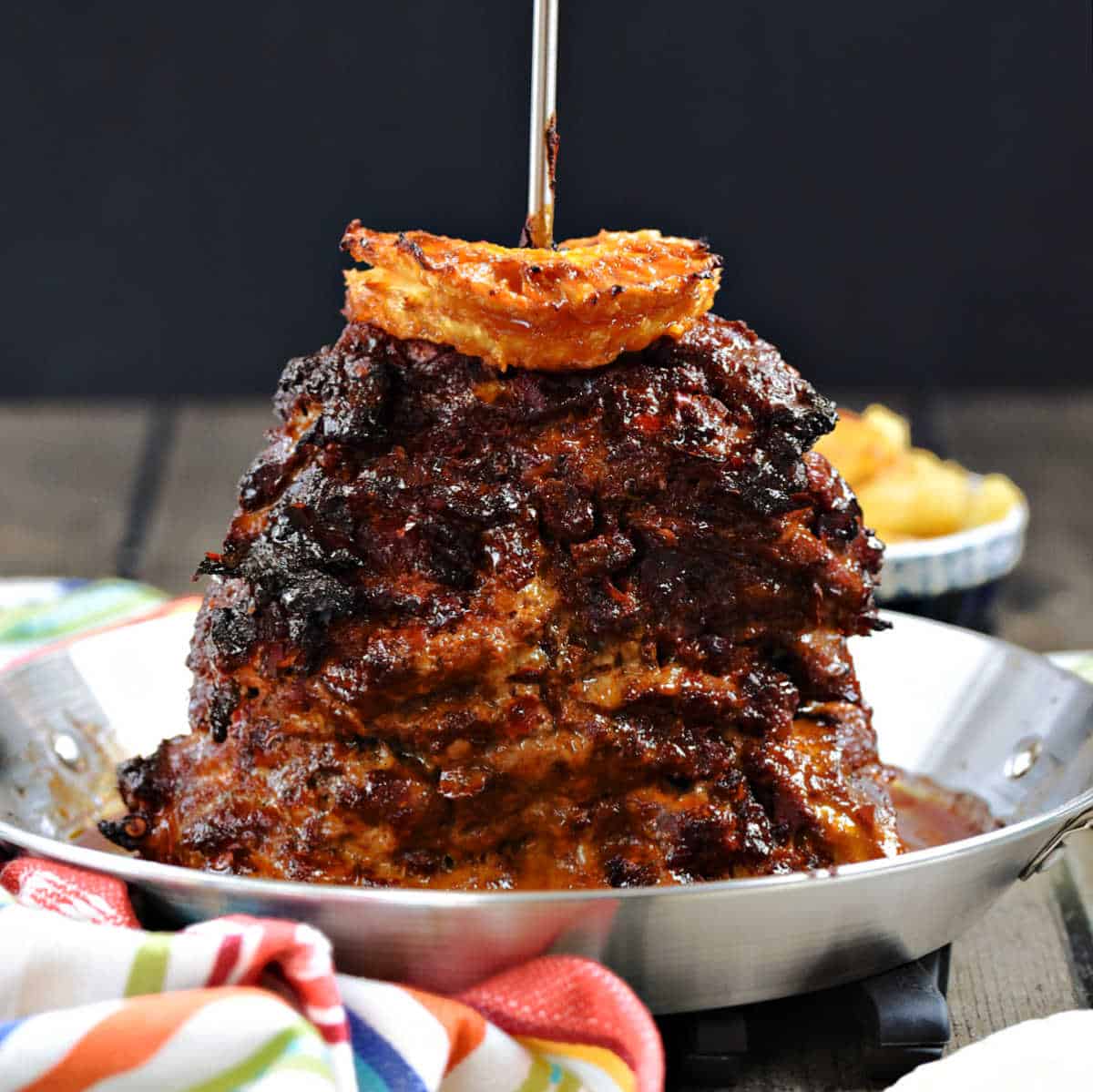 Charred, sliced pork stacked on a skewer pan topped with pineapple slices.