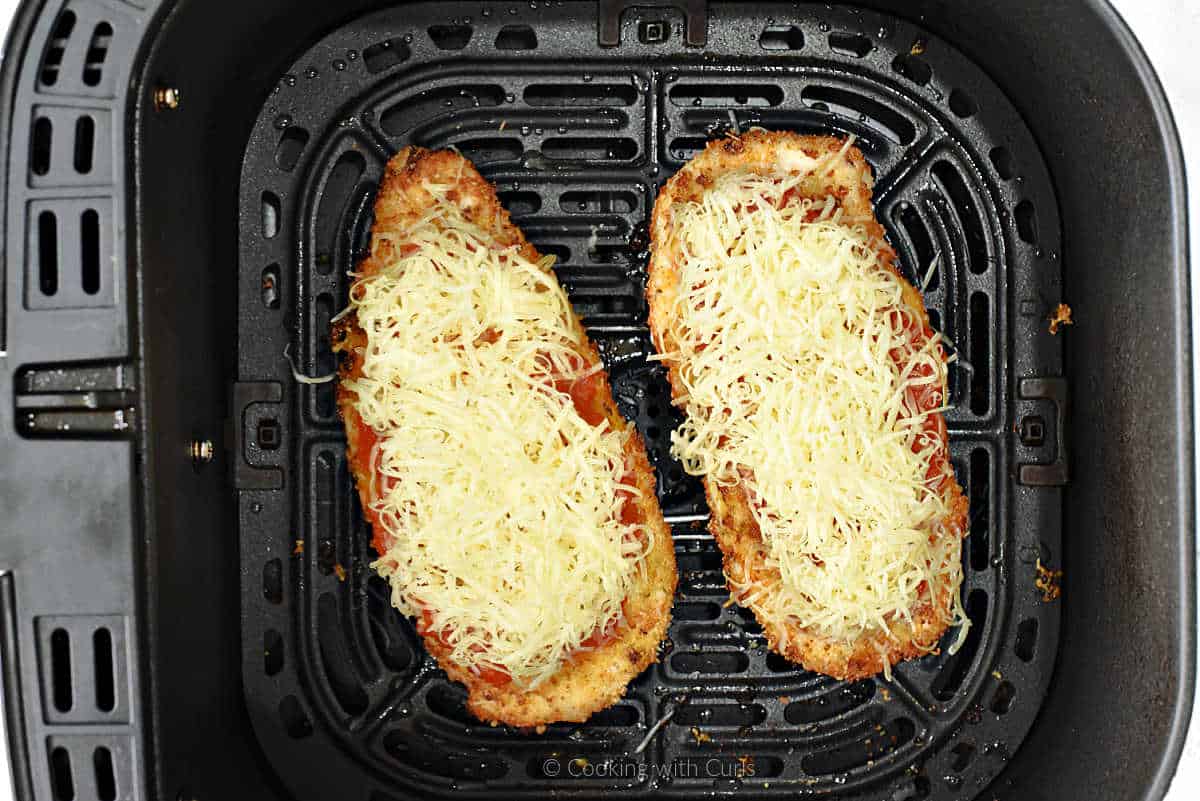 Chicken parmesan with grated mozzarella cheese in air fryer basket.